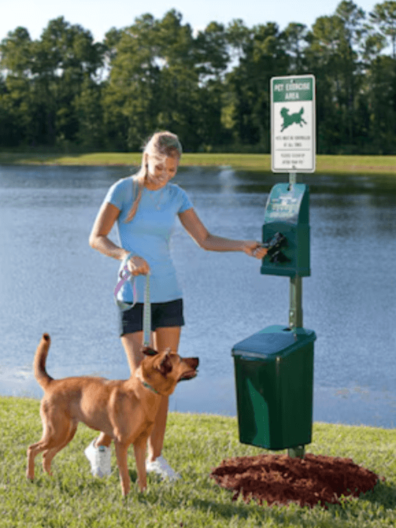 Pet owner using a waste station by a lake with their dog, demonstrating proper waste station usage and maintenance